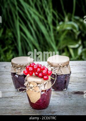 Three jars of homemade jam made from blackberries and currants on vintage wooden table in the garden. Close up with copy space. Stock Photo