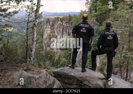 Bad Schandau, Germany. 24th July, 2020. Two officers of the Evidence and Arrest Unit of the Dresden Police Headquarters stand on a rock and look over a wooded area with sandstone rocks near the Bastei. Credit: Tino Plunert/dpa-Zentralbild/ZB/dpa/Alamy Live News Stock Photo