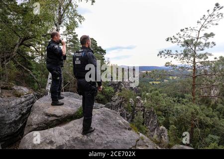 Bad Schandau, Germany. 24th July, 2020. Two officers of the Evidence and Arrest Unit of the Dresden Police Headquarters stand on rocks and look over wooded areas with sandstone rocks near the Bastei. Credit: Tino Plunert/dpa-Zentralbild/ZB/dpa/Alamy Live News Stock Photo