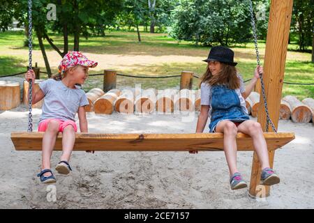 two girls ride on a bench - swing looking at each other Stock Photo