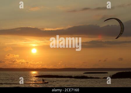 A power kite surfer swimming in the lagoon against the backdrop of a sunset, Lithuania Stock Photo