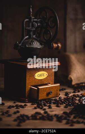 Retro coffee grinder placed on wooden table with scattered coffee beans in cafe Stock Photo