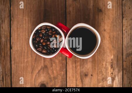 Top view composition of red cups with roasted aromatic coffee beans and fresh hot energizing americano placed together on wooden table Stock Photo