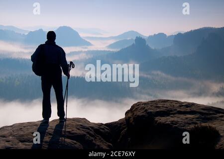 Dark silhouette of hiker with poles in hand. Sunny spring daybreak in rocky mountains. Hiker with sporty backpack stand on rocky Stock Photo