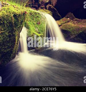 Cascade on small mountain stream. Cold crystal  water is falling over basalt mossy boulders into small pool. Stock Photo