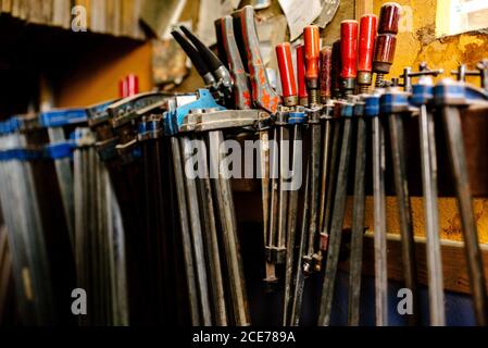 Various metal tools and clamps for woodwork placed on shelf in shabby carpentry Stock Photo