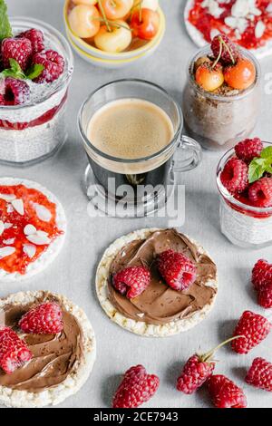 High angle of glass cup of coffee with chia pudding garnished with raspberries and white cherries with wheat crispbreads with nut spread and jam with almond pieces Stock Photo