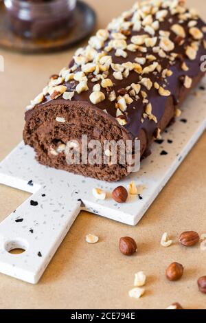 Delicious homemade roll cake with chocolate glaze and hazelnut placed on chopping board in modern kitchen Stock Photo