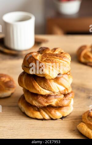 Stack of tasty cinnamon rolls placed on wooden table with cup of coffee in kitchen Stock Photo