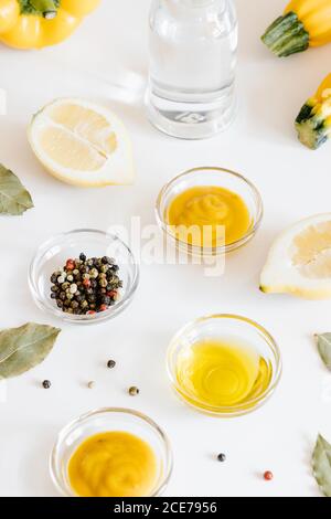 From above of tasty sauces and peppercorns in glass bowls arranged with halves of lemons and bottle of water on table Stock Photo
