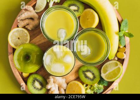 From above of glasses with healthy detox drinks with ice cubes placed on wooden tray with apple and ginger Stock Photo