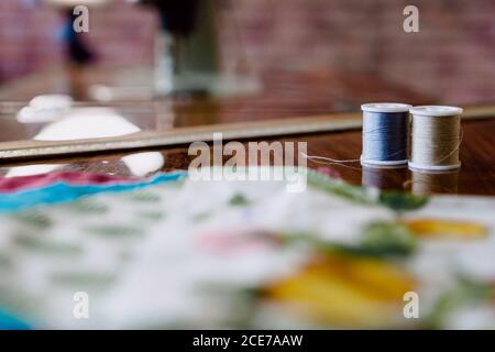 Spools of thin gray and blue threads on wooden table near soft textile samples with patterns in workshop in daylight on blurred background Stock Photo