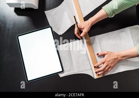 from above crop seamstress standing leaned forward while using straightedge at table with papers in studio Stock Photo