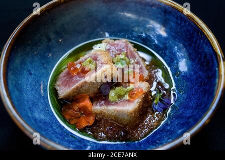From above of bowl with seared ahi tuna garnished with caviar and herbs and placed on wooden table in cafe Stock Photo