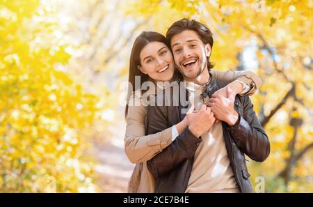 Positive woman hugging her man from behind, posing at park Stock Photo