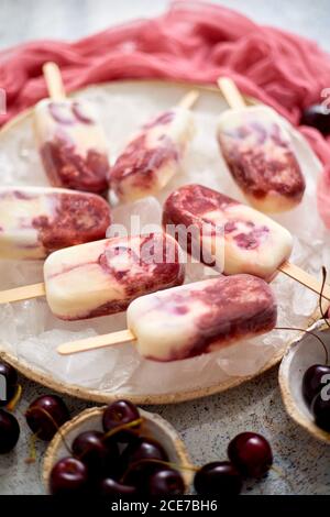 Fresh cream and cherry homemade popsicles placed on white ceramic plate with fruits and textile Stock Photo
