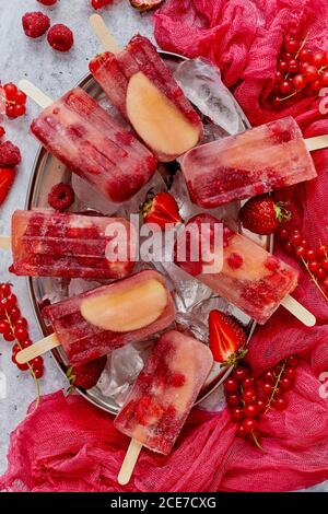 Homemade raspberry, strawberry, apple and currant popsicles on metal plate with ice assorted berries Stock Photo