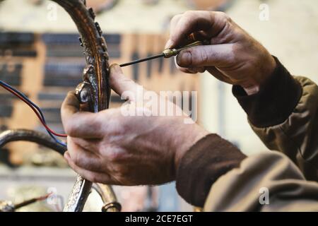 Side view of crop anonymous craftsman using screwdriver while creating metal object with ornament in studio on blurred background Stock Photo
