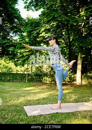 Side view of concentrated female standing in Natarajasana and practicing yoga in park on sunny day Stock Photo