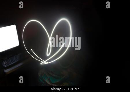 Light Forming a Love Symbol in Front of a Computer in a Dark Place Stock Photo