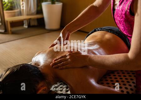 Crop anonymous master performing ayurvedic massage with aromatic oil on back of relaxed customer in modern salon Stock Photo