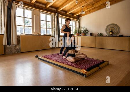 Female yoga instructor helping calm Woman practicing mindfulness in Lotus pose in studio Stock Photo