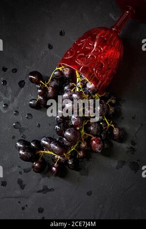 Top view of ripe juicy red grapes spilled from red wine goblet on black slate board Stock Photo