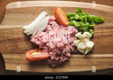 Top view of wooden cutting board with raw minced meat and chopped vegetables during preparation of traditional Italian Bolognese pasta Stock Photo