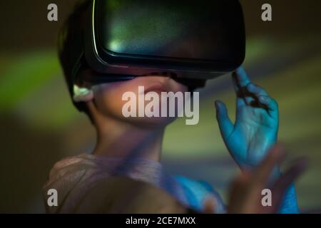Cute boy wearing VR glasses and exploring virtual reality while standing under colorful projection Stock Photo