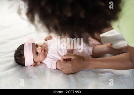 From above young African American Woman having fun with adorable newborn child lying on soft bed Stock Photo