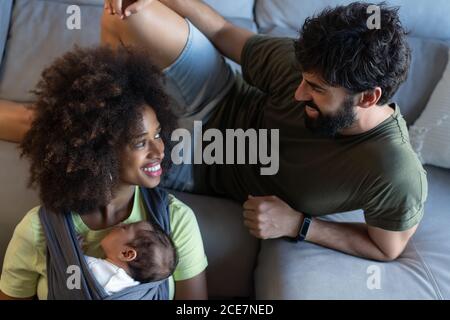 From above content multiracial mother and father playing with adorable baby while resting on floor in modern apartment Stock Photo