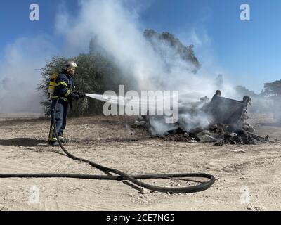 Side view of brave fireman in protective uniform standing with hose and extinguishing fire on dump in nature Stock Photo