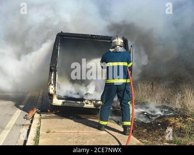Low angle back view of firefighter extinguishing fire with water hose on sunny day Stock Photo