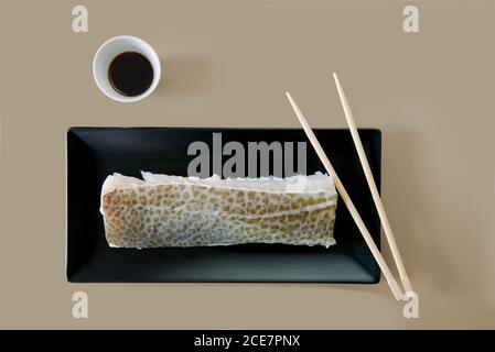 Top view of uncooked fresh fish fillet on black ceramic plate near small bowl with salty soybean sauce and wooden chopsticks on beige background Stock Photo
