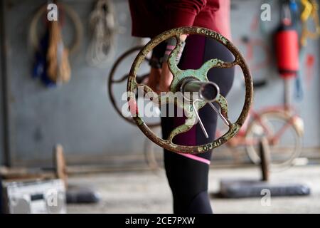 Side view of crop anonymous female bodybuilder in sportswear raising barbell with shabby and rusty pancakes while standing on floor in athletic club Stock Photo