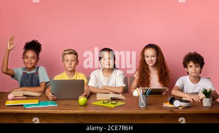 Focused black girl and her friends ready to answer lesson at desk over pink background, free space Stock Photo