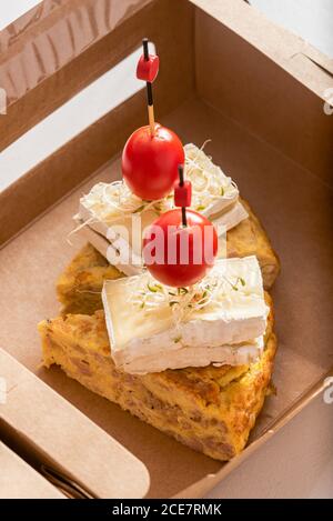 High angle closeup of delicious omelette garnished with cheese and cherry tomatoes and placed in eco friendly cardboard box Stock Photo