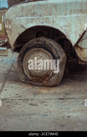 Closeup of old fashioned automobile with flat tyre and dirty surface with damaged paint coating parked on asphalt road in city in daylight Stock Photo