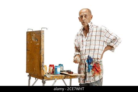 Male caucasian artist, painter at work isolated on white studio background. Painting, working with colors, making composition. Concept of professional occupation, work, job, craft production. Stock Photo