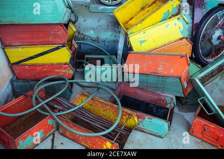 From above of heap of used colorful rectangular metal boxes with shabby and rusty surface near cable and bike wheel on floor in garage Stock Photo