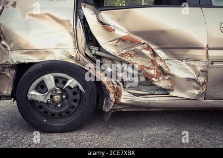 Modern car with dent on back door with rusty surface and partially broken metal wheel rim parked on pavement in city street Stock Photo