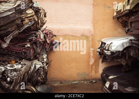 Dump of heap of ruined dirty multicolored autos after accident put on wet pavement near concrete wall Stock Photo