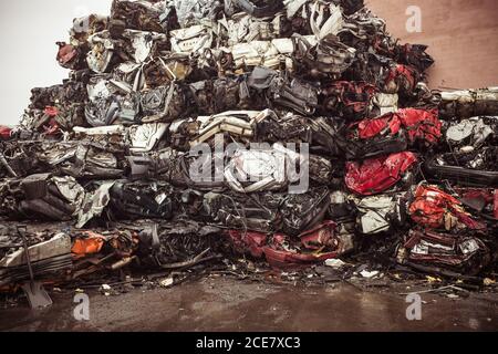 Dump of heap of ruined dirty multicolored autos after accident put on wet pavement near concrete wall Stock Photo