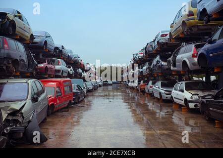 Rubbish dump with pile of multicolored modern automobiles after accident with dents on surface on wet road under blue sky in town Stock Photo