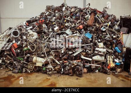 Dump of pile of different old multicolored metal parts for recycling on brown floor near cement wall Stock Photo