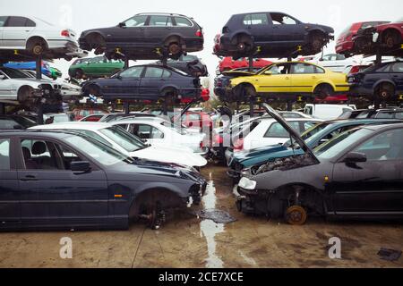 Rubbish dump with pile of multicolored modern automobiles after accident with dents on surface on wet road under blue sky in town Stock Photo