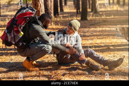 Black guy helping his injured friend, hiking together Stock Photo