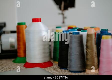 High angle of various colorful cotton threads on spools arranged on table near sewing machine at workplace of seamstress Stock Photo