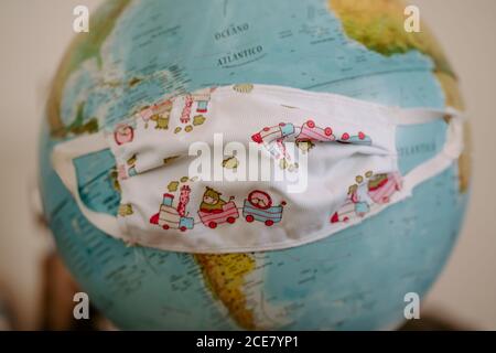 Handmade mask for coronavirus protection made from fabric with colorful infant print placed on globe Stock Photo
