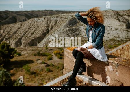 Side view of African American female sitting on edge of old building and admiring amazing landscape in summer Stock Photo